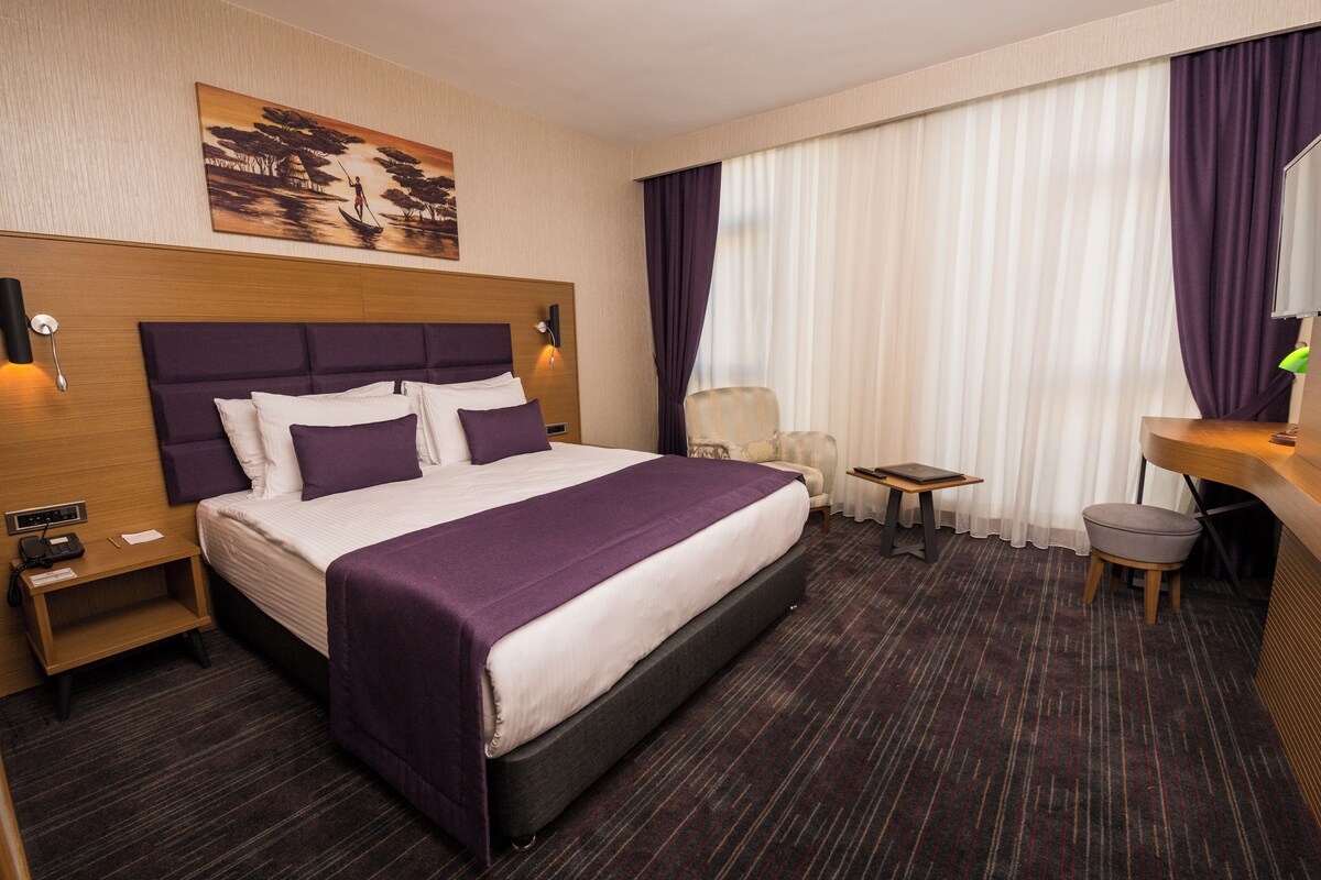 A hotel room with a large bed, a desk, a chair, and a small table.