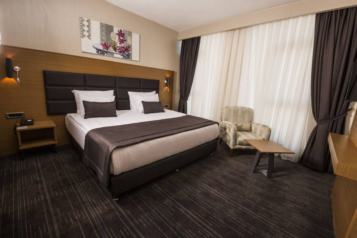 Een hotelkamer met een groot bed, een nachtkastje, een stoel, een kleine tafel en een aan de muur bevestigde televisie.