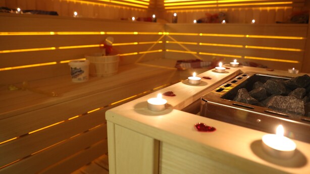 Un sauna avec des bancs en bois, de nombreuses bougies et un élément chauffant en pierre.