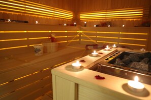 Eine Sauna mit Holzbänken, zahlreichen Kerzen und einem Steinofen.