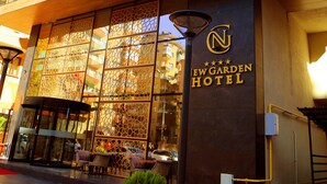 L’extérieur du New Garden Hotel présente un design moderne, de grandes fenêtres et un espace d’entrée bien visible, agrémenté d’un coin salon extérieur.