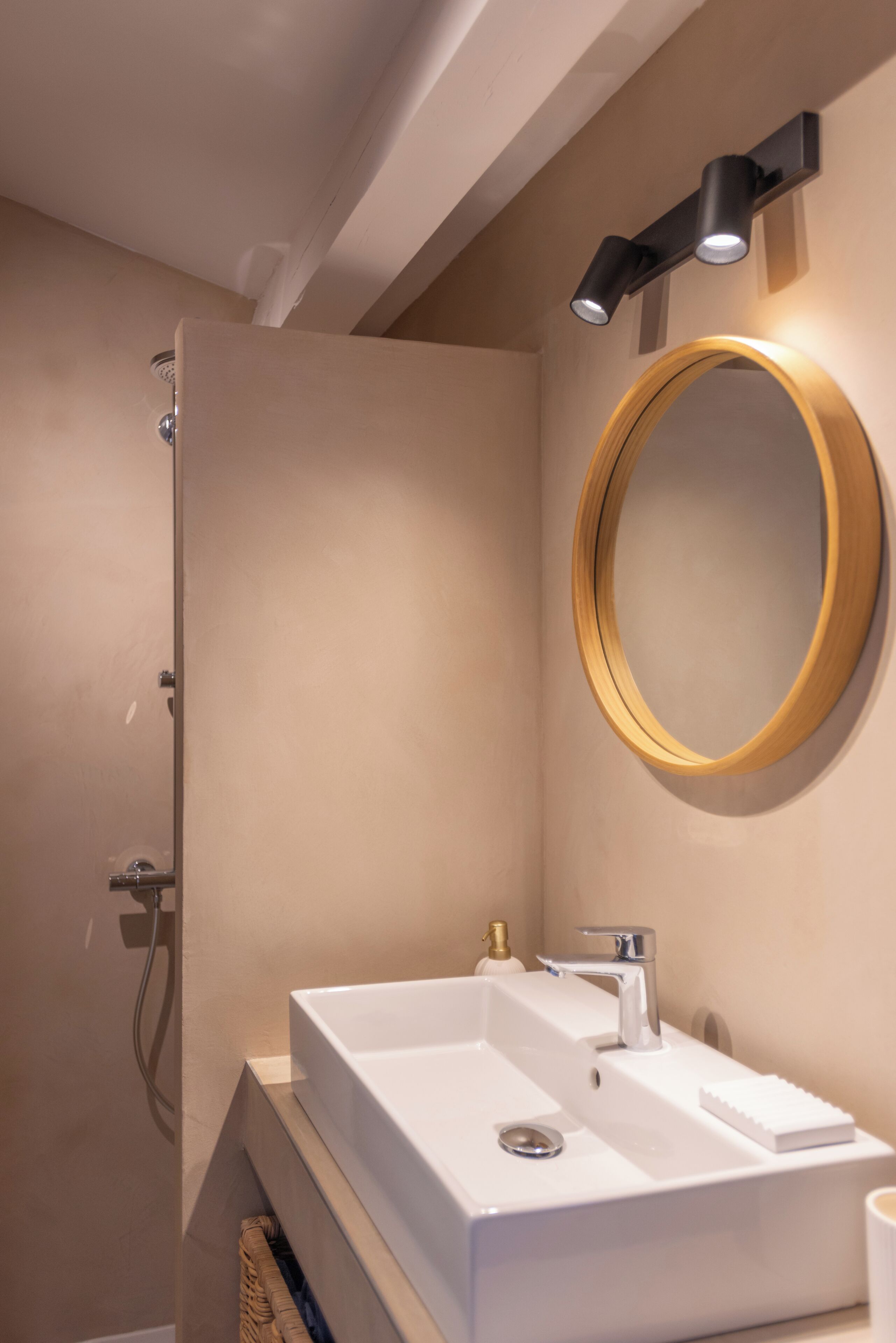 Un baño moderno con un lavamanos blanco, un espejo redondo y una ducha.
