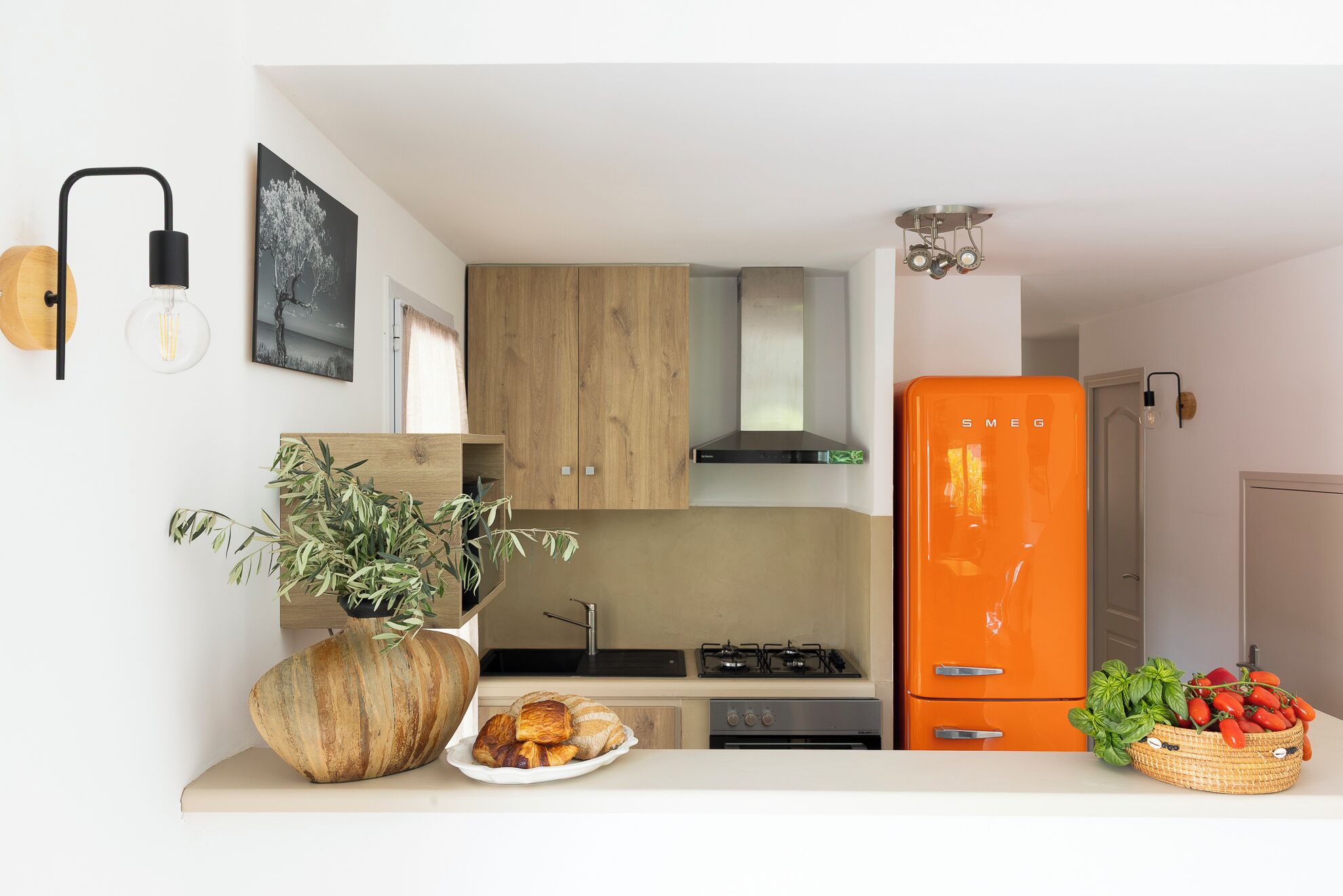 Una cucina compatta con mobili in legno, un piano cottura a gas moderno e un frigorifero arancione in stile retrò.