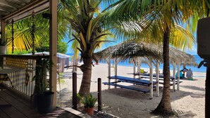 A beachside area with thatched umbrellas, wooden benches, and potted plants. - Anse des rochers - Studio Cashew (saint-françois)