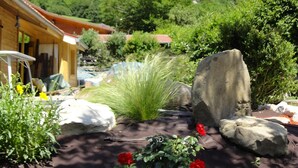 Jardí amb una pedra central, flors vermelles i una muntanya al fons.
