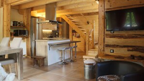 Interior d'una cabana de fusta amb cuina, zona de menjador i una escala.