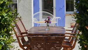 An outdoor seating area with a round table and wooden chairs, surrounded by greenery.