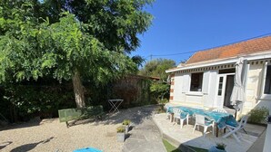Un patio con mesa y sillas, un banco verde y un pequeño jardín con plantas en macetas.