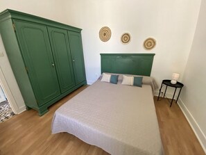A bedroom with a bed, a green wardrobe, a bedside table with a lamp, and three wall decorations.