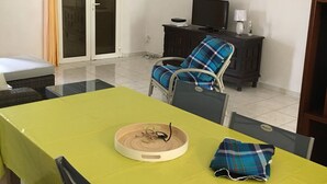 A dining area with a green table, chairs, a television, and a sliding glass door. - HIBISCUS HOUSE 2 LARGE BEDROOMS with bathroom (Le Gosier)