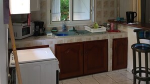 A kitchen with a white refrigerator, a microwave, a coffee maker, and a sink. There is a window with a view of greenery outside. - HIBISCUS HOUSE 2 LARGE BEDROOMS with bathroom (Le Gosier)