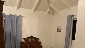 A bedroom with a wooden bed, a nightstand, and a window with curtains. - HIBISCUS HOUSE 2 LARGE BEDROOMS with bathroom (Le Gosier)