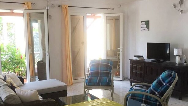 A living room with a sofa, two armchairs, a TV, and a sliding glass door leading to a balcony. - HIBISCUS HOUSE 2 LARGE BEDROOMS with bathroom (Le Gosier)