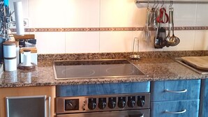 Una cocina con estufa, horno y campana de acero inoxidable. Hay armarios con pomos, una encimera con fregadero y un salpicadero.
