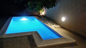 Una piscina rectangular de color azul claro, rodeada por un borde de piedra y una capa de piedras pequeñas en un lado.