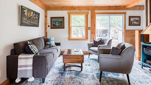 Ein gemütliches Wohnzimmer mit Holzbalkendecke, einer Couch, einem Sessel und einem Couchtisch.