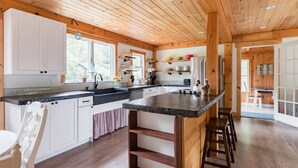 Eine moderne Küche mit Holzbalken, weißen Schränken, einer zentralen Kochinsel mit Barhocker und einem Essbereich mit Tisch und Stühlen.