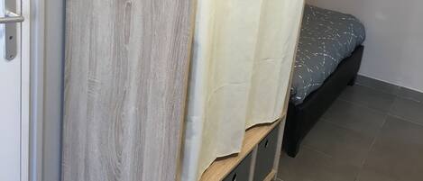 A room with a bed, a wooden wardrobe, and a curtain.