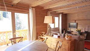 A wooden cabin interior with a dining table, chairs, a kitchen area with a sink, and a television. - 3 room duplex (97m²) - Méribel Le Plantin - Hameau des Biches (Les Allues)