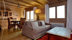 A cozy cabin interior with a wooden ceiling, a sofa, a dining table, and a window with curtains. - 3 room duplex (97m²) - Méribel Le Plantin - Hameau des Biches (Les Allues)