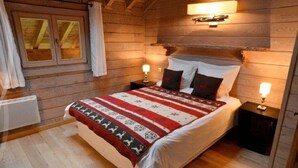 A cozy wooden cabin bedroom with a large bed, two bedside tables, and a window with curtains. - 3 room duplex (97m²) - Méribel Le Plantin - Hameau des Biches (Les Allues)