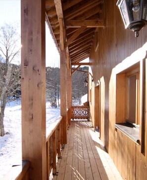 A wooden cabin with a covered porch and a window with a view of the snowy landscape.