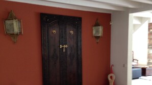 Une pièce dotée d’une porte en bois sombre, de deux lanternes fixées aux murs et d’un tapis à motifs.