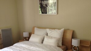 Un lit bien fait, avec du linge de lit blanc, une tête de lit en bois et deux tables de chevet avec des lampes.