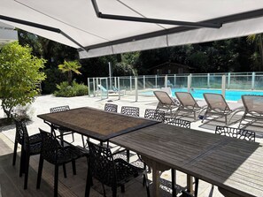 An outdoor patio area with a pool, covered seating, and a table with chairs.