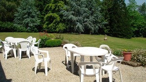 An outdoor seating area with white plastic chairs and tables, surrounded by a gravel surface and a well-maintained lawn. - Morbihan 15 km sea, beautiful farmhouse 9personnes (Berric)