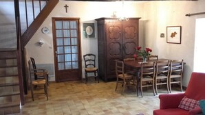 A cozy living room with a wooden staircase, a dining table with chairs, a red armchair, and a cabinet with a floral design. - Morbihan 15 km sea, beautiful farmhouse 9personnes (Berric)