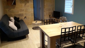 Una sala de estar acogedora con un sofá azul oscuro, una mesita redonda con un vaso y un televisor sobre un mueble de madera.