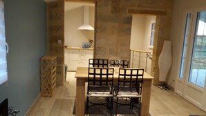 Un comedor con mesa y sillas de madera, una cocina al fondo y un ventanal con persianas.