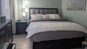 A bedroom with a bed, nightstands, a dresser, and a wall-mounted lamp. - Spacious Sunny Apt: Walk to Shop, Eat & NYC Train (Montclair)