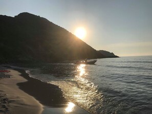 A beach with a boat, calm water, and a sunlit hill in the background. - CASA ROSSA - VILLA **** - Heated swimming pool - Near L'Ile-Rousse beach (MONTICELLO)