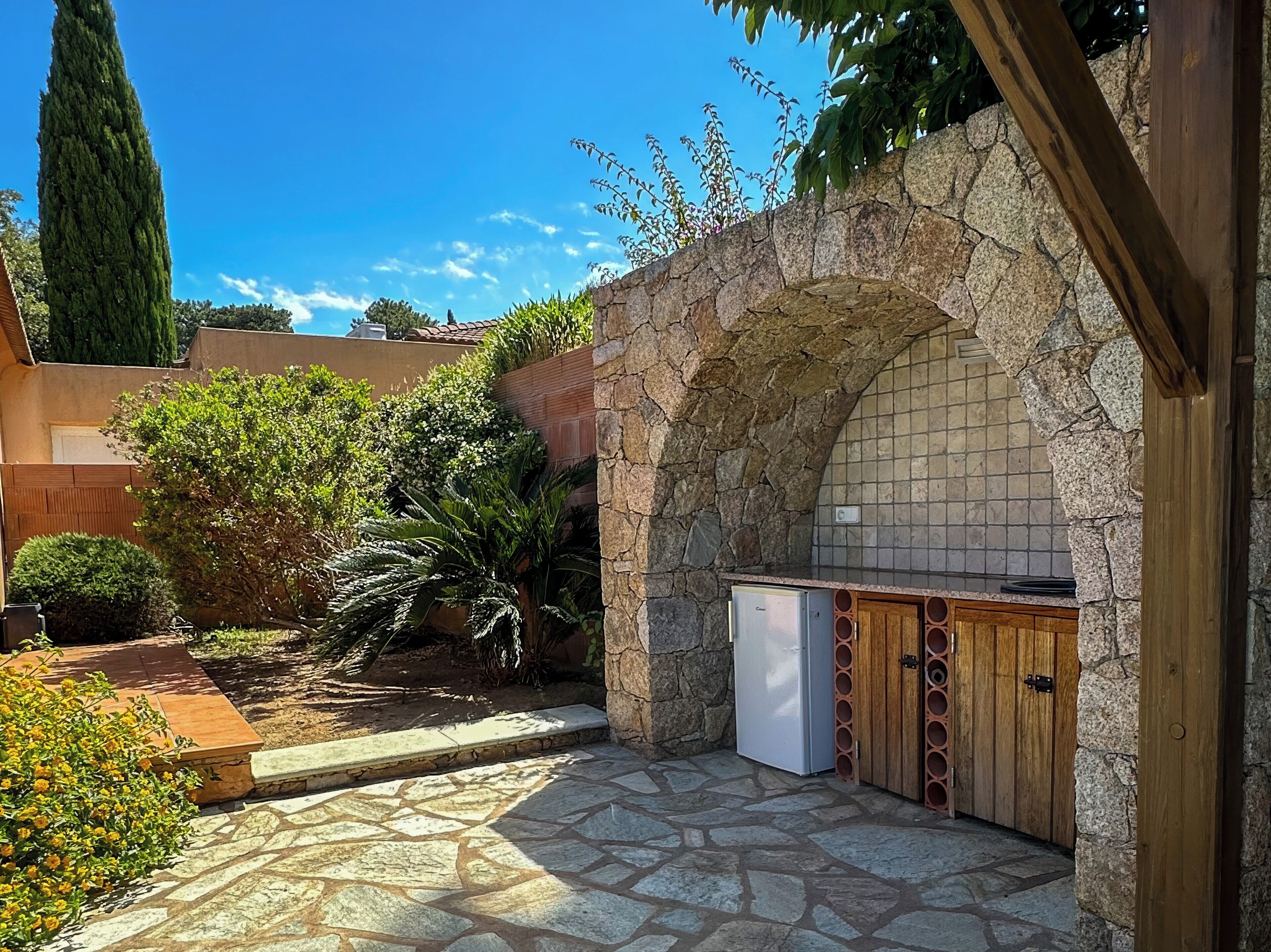 A stone archway leading to a kitchen with a stone floor and a small refrigerator.