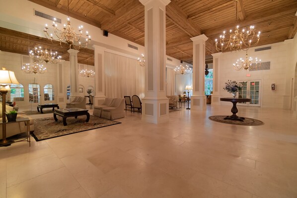A spacious lobby with high ceilings, chandeliers, and a central seating area with sofas and a coffee table.