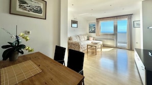 Una sala de estar moderna con comedor, un sofá, una mesa de centro y vista al mar a través de un amplio ventanal.