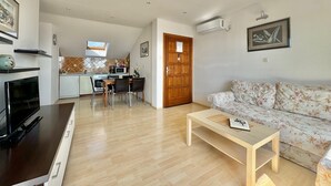 Una sala de estar moderna con sofá, mesa de centro, televisor y cocina al fondo.