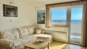 Un salón con sofá, una mesa de centro, un cuadro enmarcado y una ventana con vistas al mar.