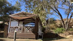 Una piccola baita di legno con veranda, circondata da alberi e erba secca.
