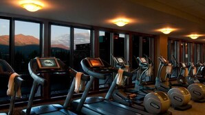 A gym with treadmills and ellipticals, large windows with a mountain view, and ceiling lights.