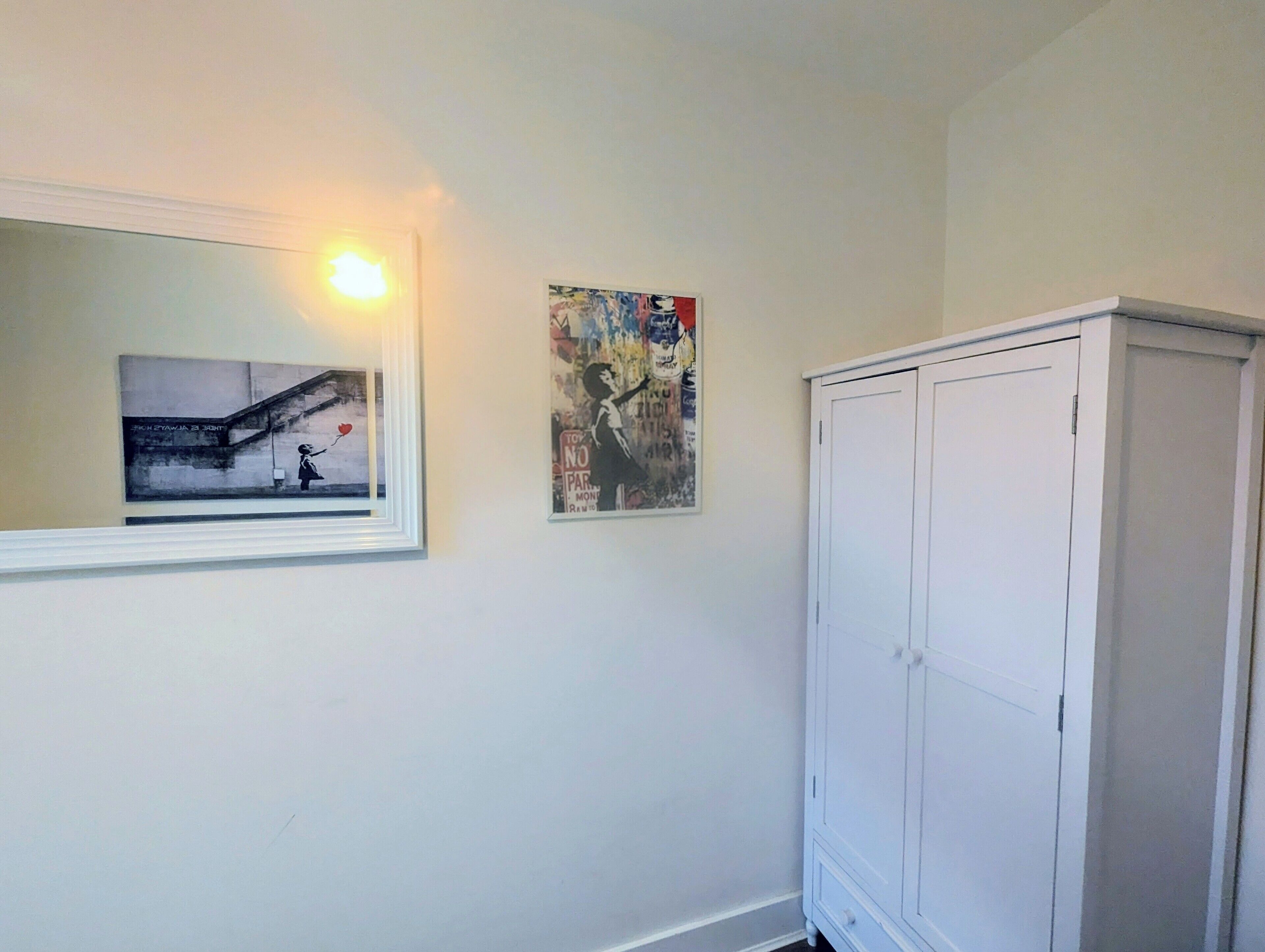 A room with a white wardrobe, a framed picture on the wall, and a window with a light fixture.