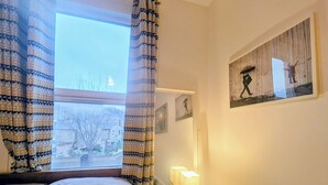 Une chambre à coucher avec un lit, une table de chevet avec une lampe, une horloge et une fenêtre avec des rideaux.