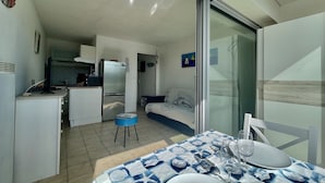 A compact living space with a kitchenette, a dining area with a table set for two, and a bedroom with a bed and a nightstand. - "All Baigne" - 1CH apartment with loggia closed sea panorama (Quiberon)