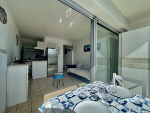 A compact living space with a kitchenette, a dining area with a table set for two, and a bedroom with a bed and a nightstand.