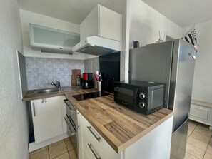 Cocina compacta con armarios blancos, encimera de madera, microondas integrado, refrigerador de acero inoxidable y estufa a gas.