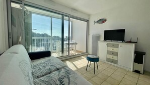 A modern room with a large sliding glass door leading to a balcony, a flat-screen TV, a small stool, and a white cabinet. - "All Baigne" - 1CH apartment with loggia closed sea panorama (Quiberon)