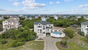 A large, two-story house with a front porch, a swimming pool, and a well-maintained lawn. - 1522 - Sand Dollar - Oceanside Corolla Home w/ Pool & Volleyball (Corolla)