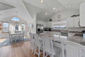 A spacious kitchen with white cabinetry, a large island, and a dining area with white chairs.